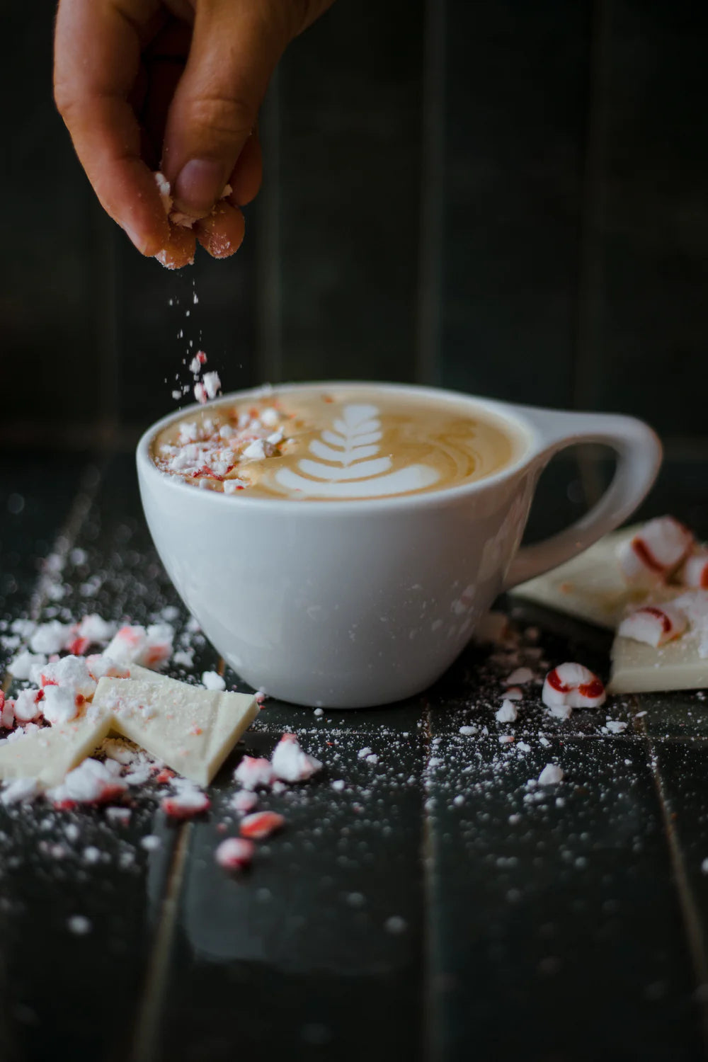 A festive latte topped with peppermint sprinkles and latte art at Cottonwood Coffee, surrounded by crushed candy canes and white chocolate pieces.